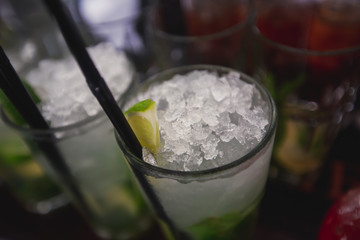 Beautiful row line of different colored alcohol cocktails on a party, martini, vodka,and others on decorated catering bouquet table on open air event, picture with beautiful bokeh
