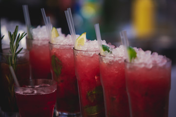 Beautiful row line of different colored alcohol cocktails on a party, martini, vodka,and others on decorated catering bouquet table on open air event, picture with beautiful bokeh
