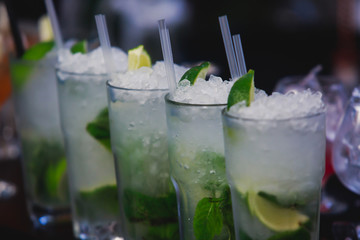 Beautiful row line of different colored alcohol cocktails on a party, martini, vodka,and others on decorated catering bouquet table on open air event, picture with beautiful bokeh
