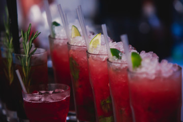 Beautiful row line of different colored alcohol cocktails on a party, martini, vodka,and others on decorated catering bouquet table on open air event, picture with beautiful bokeh
