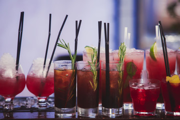 Beautiful row line of different colored alcohol cocktails on a party, martini, vodka,and others on decorated catering bouquet table on open air event, picture with beautiful bokeh
