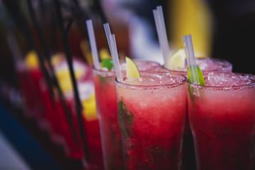 Beautiful row line of different colored alcohol cocktails on a party, martini, vodka,and others on decorated catering bouquet table on open air event, picture with beautiful bokeh
