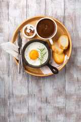 Pan of fried egg, crispy baguette fruit jam and cup of coffee on white rustic wooden table, top view. Breakfast time