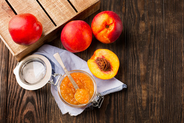 Jar of homemade peach jam with fresh fruits on rustic wooden table, top view