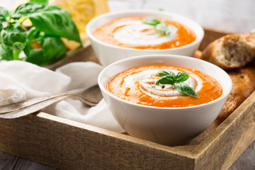 Homemade pumpkin soup with cream, fresh bread and basil on rustic wooden background, selective focus