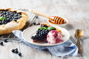 Rustic berry crispy blueberry pie with ice cream and mint on white wooden table, selective focus