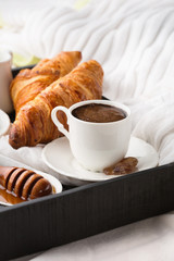Morning breakfast in bed with cup of coffee, croissants and honey on wooden tray, selective focus