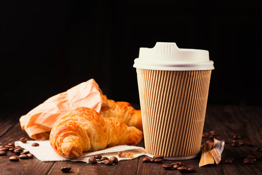 Coffee to go in a paper cup with croissants on wooden table, selective focus