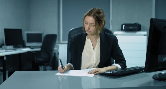 4K: Eine junge Angestellte arbeitet in einem B&uuml;ro. Sie analysiert einige Finanzberichte und gibt ihre Unterschrift zur Einwilligung.