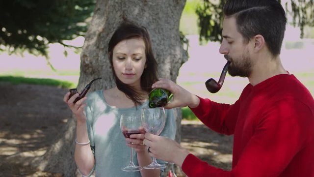 Couple smoking pipe in park and drinking wine