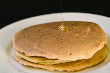 Close up of a bunch of tasty american pancakes and maple syrup poured over them. Selective focus.