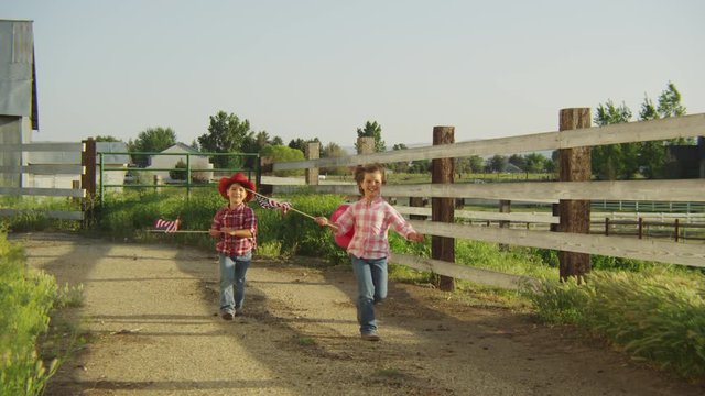 Two young cowgirls running and waving American flag