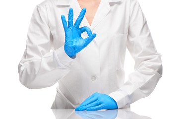 Doctor in white gown and blue gloves showing OK sign