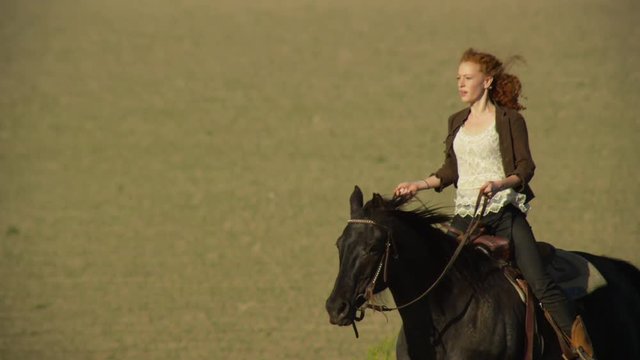 Young woman riding large horse through a farm