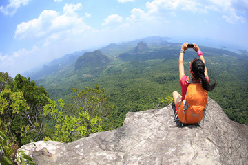 young woman hiker taking photo with smartphone on mountain peak cliff