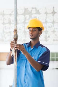 indian male plumber on site using hammer