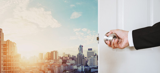 Businessman hand holding door knob opening, with Bangkok cityscape in sunrise