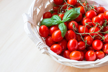 Small red cherry tomatoes in a wicker basket on an old wooden table