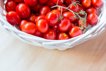 Small red cherry tomatoes in a wicker basket on an old wooden table