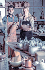man and woman potters holding ceramic vessels in atelier