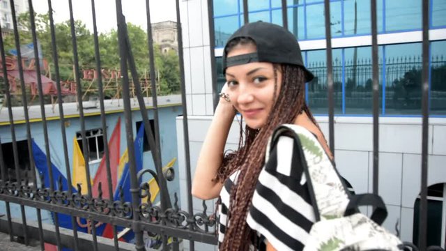 Young woman with dreadlocks and cap walks by street