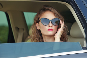 Portrait of pretty young woman in sunglasses sitting inside car