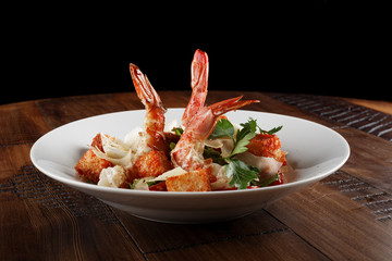 Caesar salad with king prawns in a white plate. Salad with shrimp on wooden brown background.