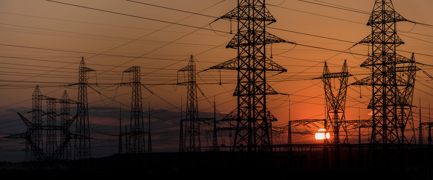 High voltage electric tower line. Electricity transmission pylon silhouetted against sunset sky. 