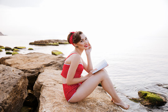 Smiling pin up girl reading book sitting on the rock