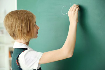 Cute schoolgirl writing on chalkboard