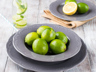 Whole green limes in a plate on rustic wooden background