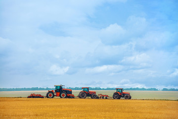 Obraz premium Summer day three tractor with plow standing on the sloping wheat field before the beginning of the work. Land preparation before planting.