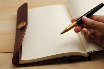 women hand with pen writing diary on wood table in warm tone background