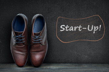 Start-up text on black board and business shoes