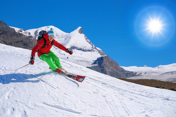 Skier skiing downhill in high mountains against sunshine