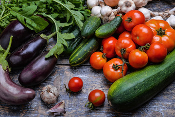 Harvest Vegetables: tomatoes, cucumbers, zucchini, eggplant, onion, garlic, arugula on the wooden background