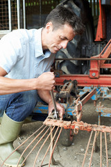 Farmer Working On Agricultural Equipment In Barn