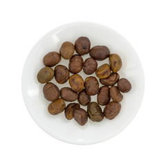 Plate of organic whole shelled roasted chestnuts top view on a white background.