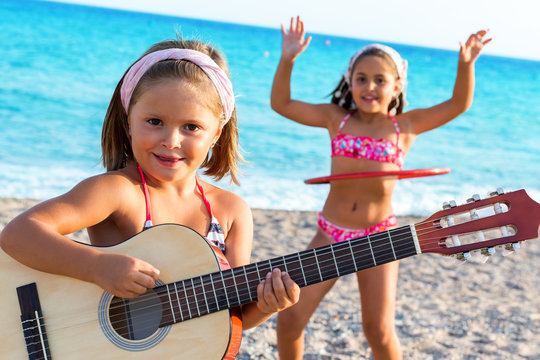 Cute girl playing guitar with friend dancing in background.