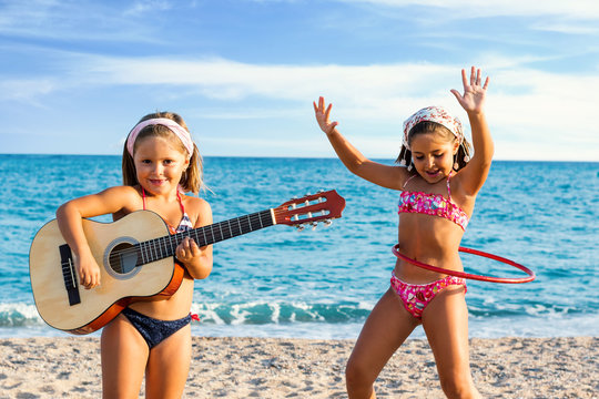 Kids dancing and singing with guitar on beach.