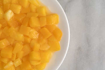 Diced mangoes on a white plate atop a marble counter top.