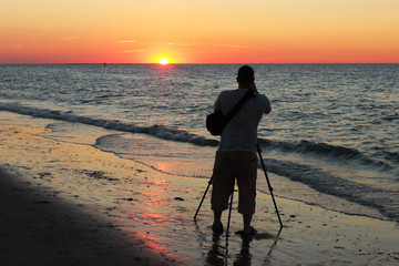 Mann fotografiert Sonnenuntergang am Meer mit Kamera auf Stativ auf Seeland in NL

