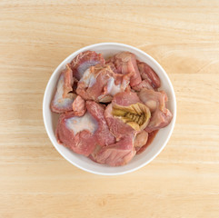 Bowl of fresh chicken gizzards and hearts on a wood table top.