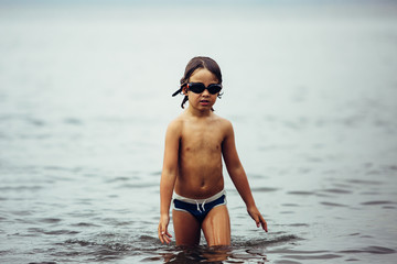 Wet-haired kid in goggles walking in sea © click_and_photo
