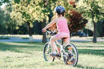 Little brunette girl riding bicycle in the park at sunset