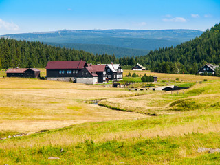 Large green meadows and rural mountain houses of Jizerka Village with Giant Mountains, or Krkonose, on the background, Jizera Mountains, Czech Republic.