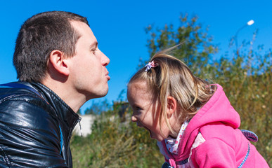 Dad tries to kiss a girl. She is laughing. in the park.  in  pink coat