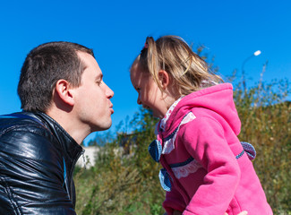 Dad tries to kiss a girl. She is laughing. in the park. in pink coat