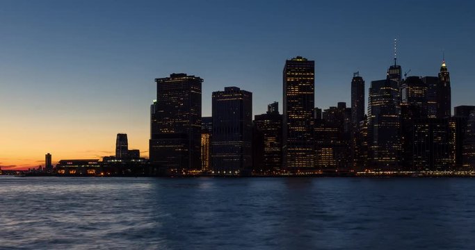 New York City skyscrapers between sunset and dusk with city lights. Time lapse cityscape view of Lower Manhattan Financial District and East River