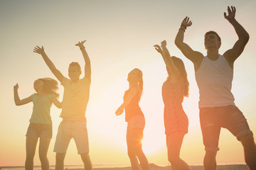 smiling friends dancing on summer beach